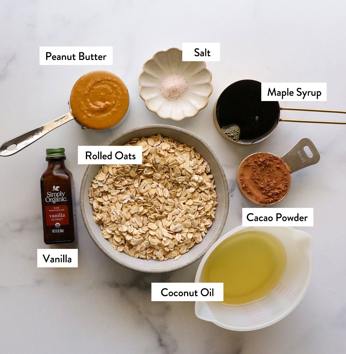 rolled oats, coconut oil, peanut butter, maple syrup, and cacao powder labeled in cups.