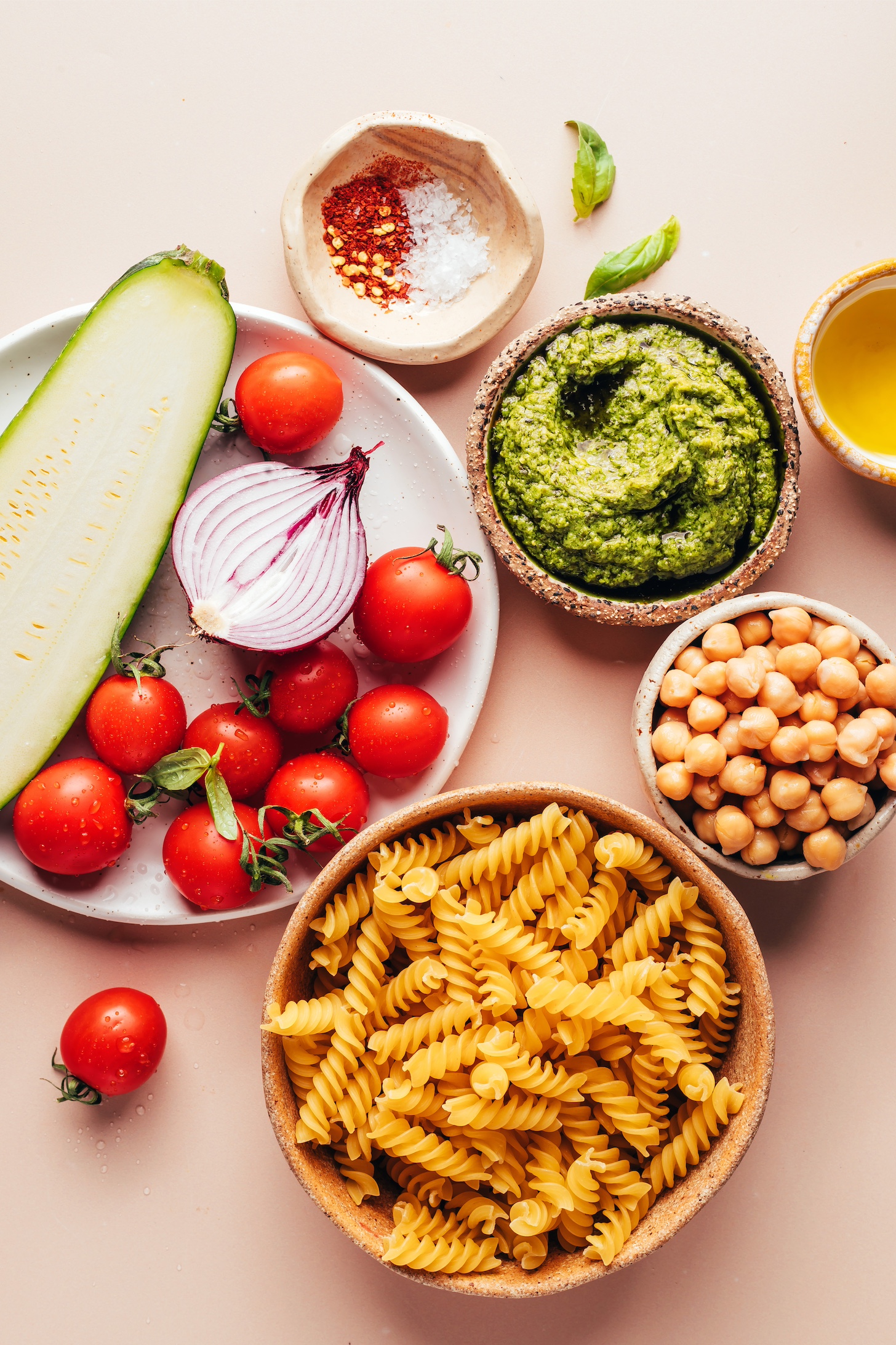 Pasta, chickpeas, pesto, olive oil, salt, red pepper flakes, cherry tomatoes, red onion, and zucchini