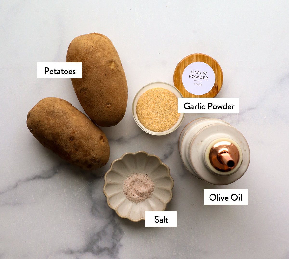russet potatoes, salt, garlic powder, and olive oil labeled on a white surface.