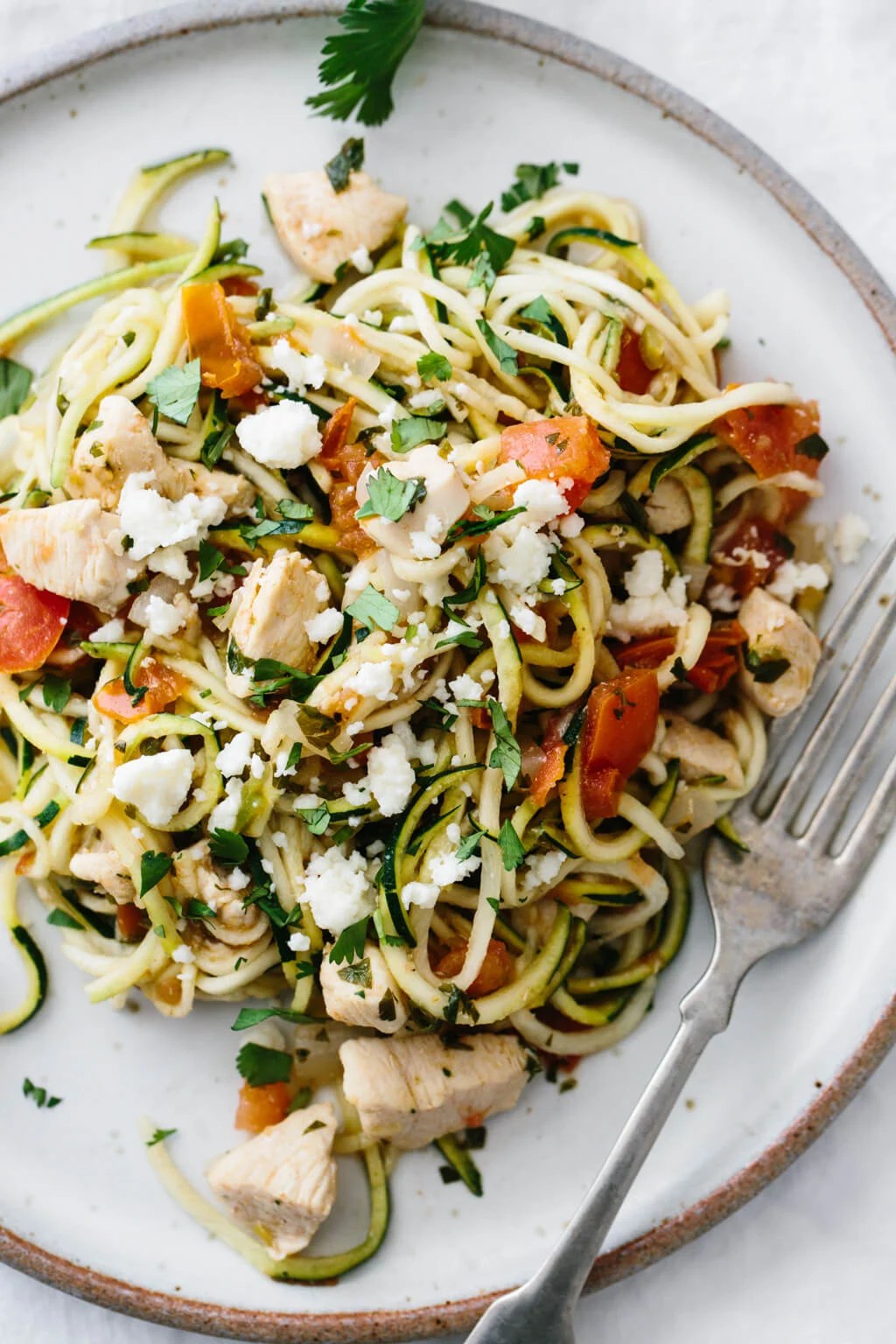 Close up of zucchini noodles with chicken and pico de gallo on a white plate.