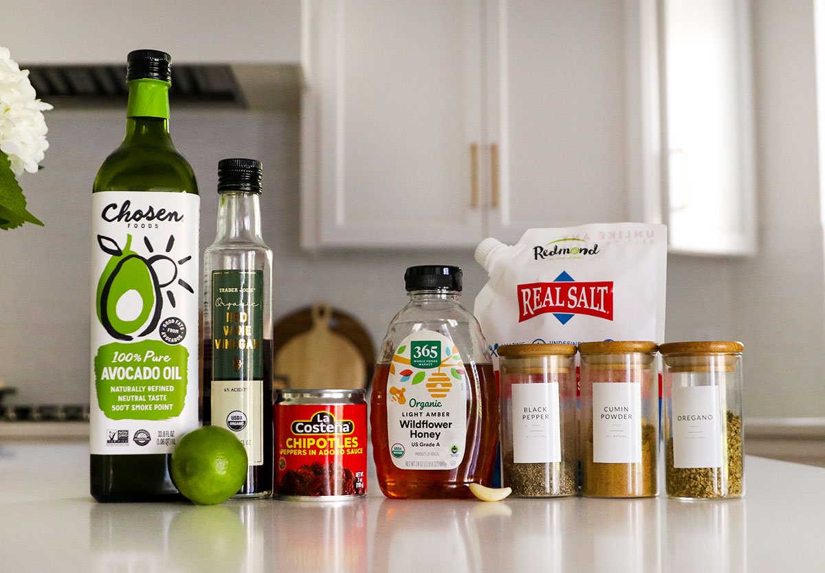 bottles of oil, vinegar, honey, and spices sitting on a white counter.