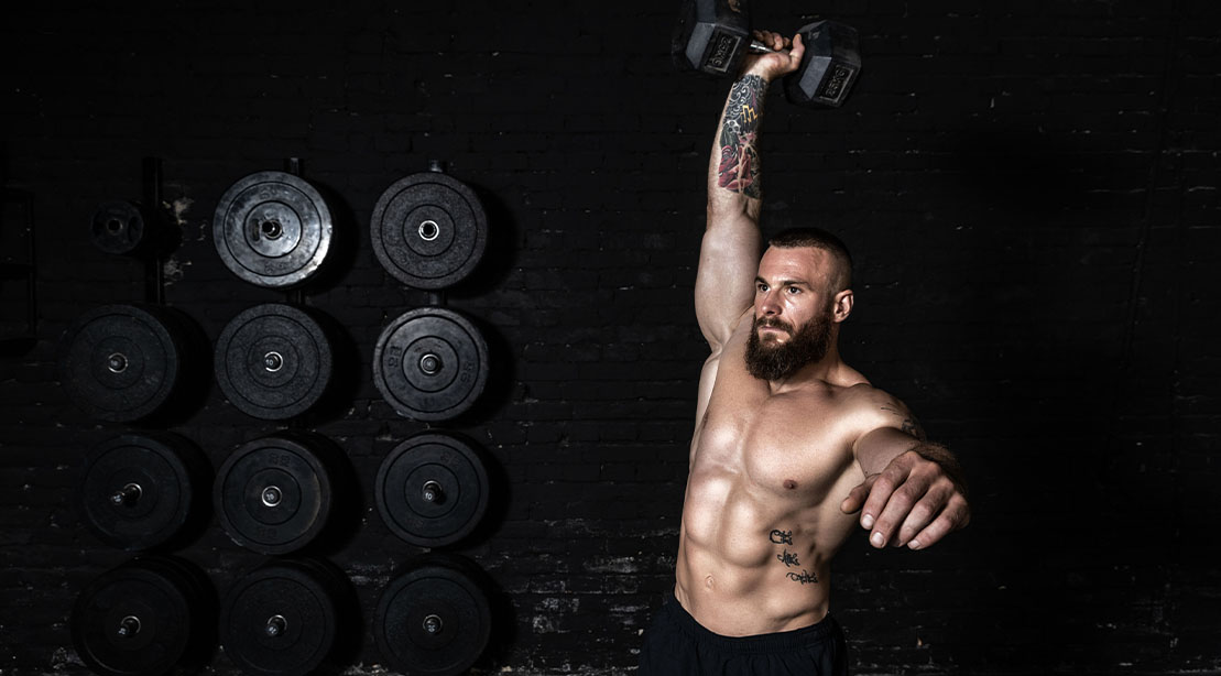 Muscular fit man performing a jerk and snatch exercise as part of his 5x5 workout method routine