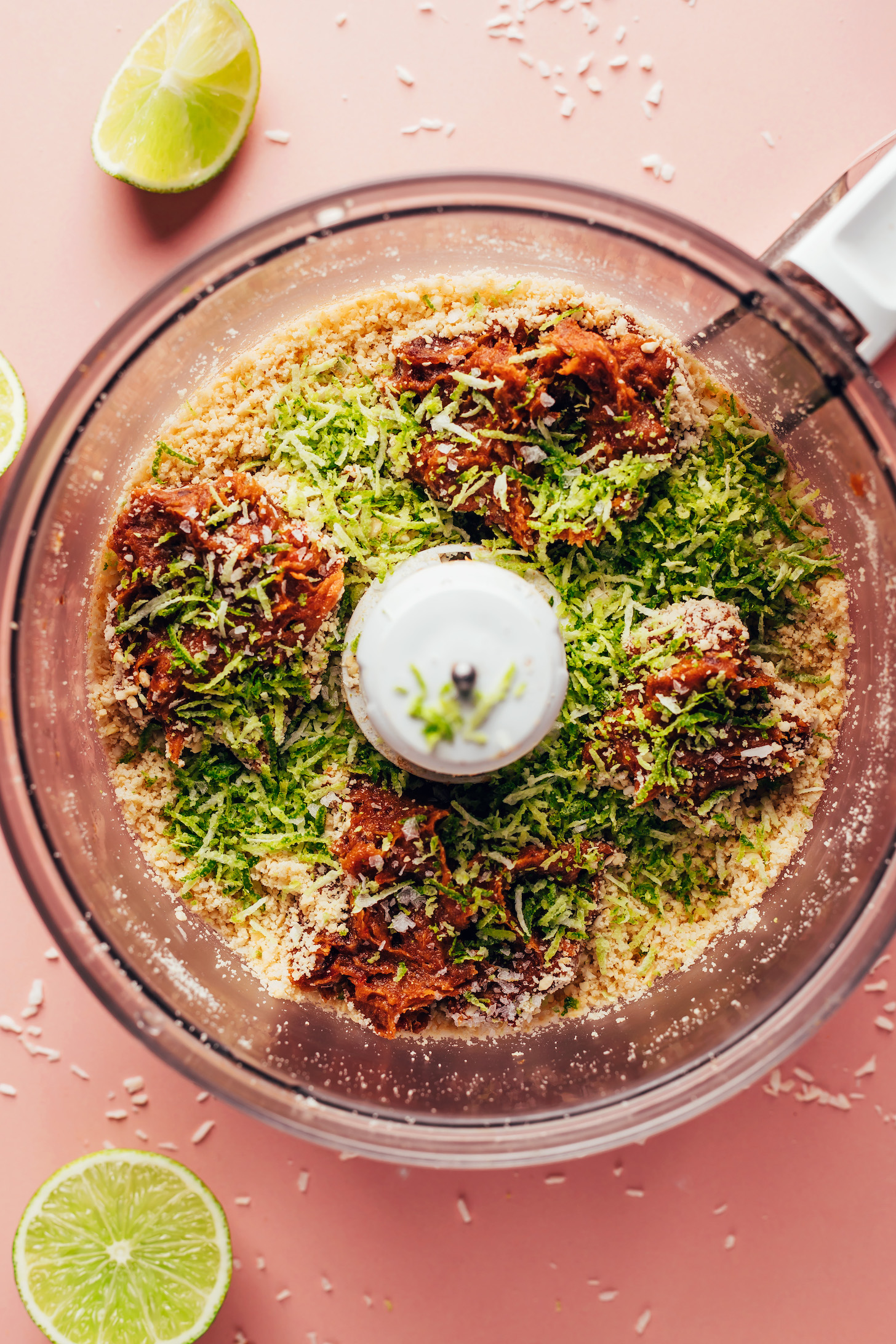 Food processor with date paste, lime zest, shredded coconut, cashews, and other ingredients for making energy bites
