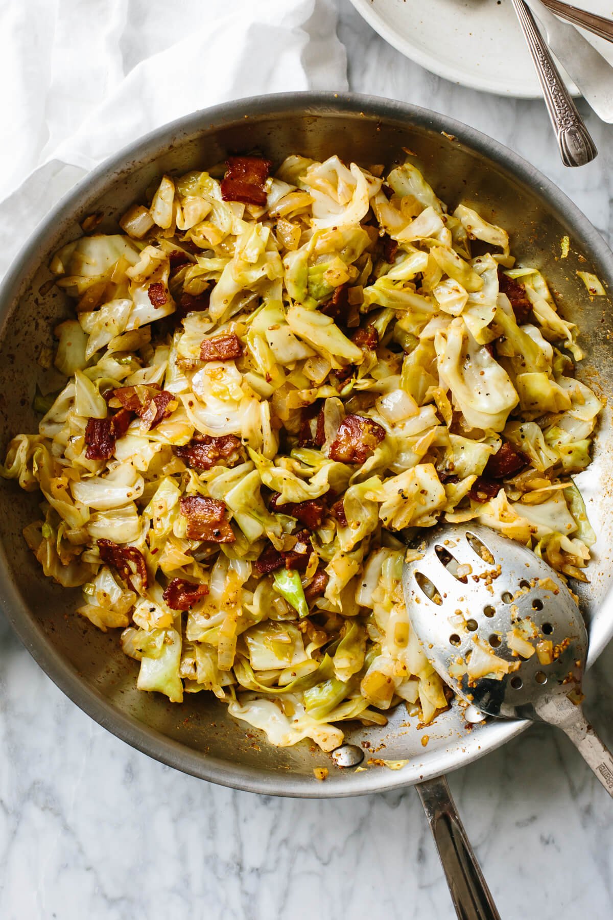 A pan with fried cabbage and a large serving spoon on a table.