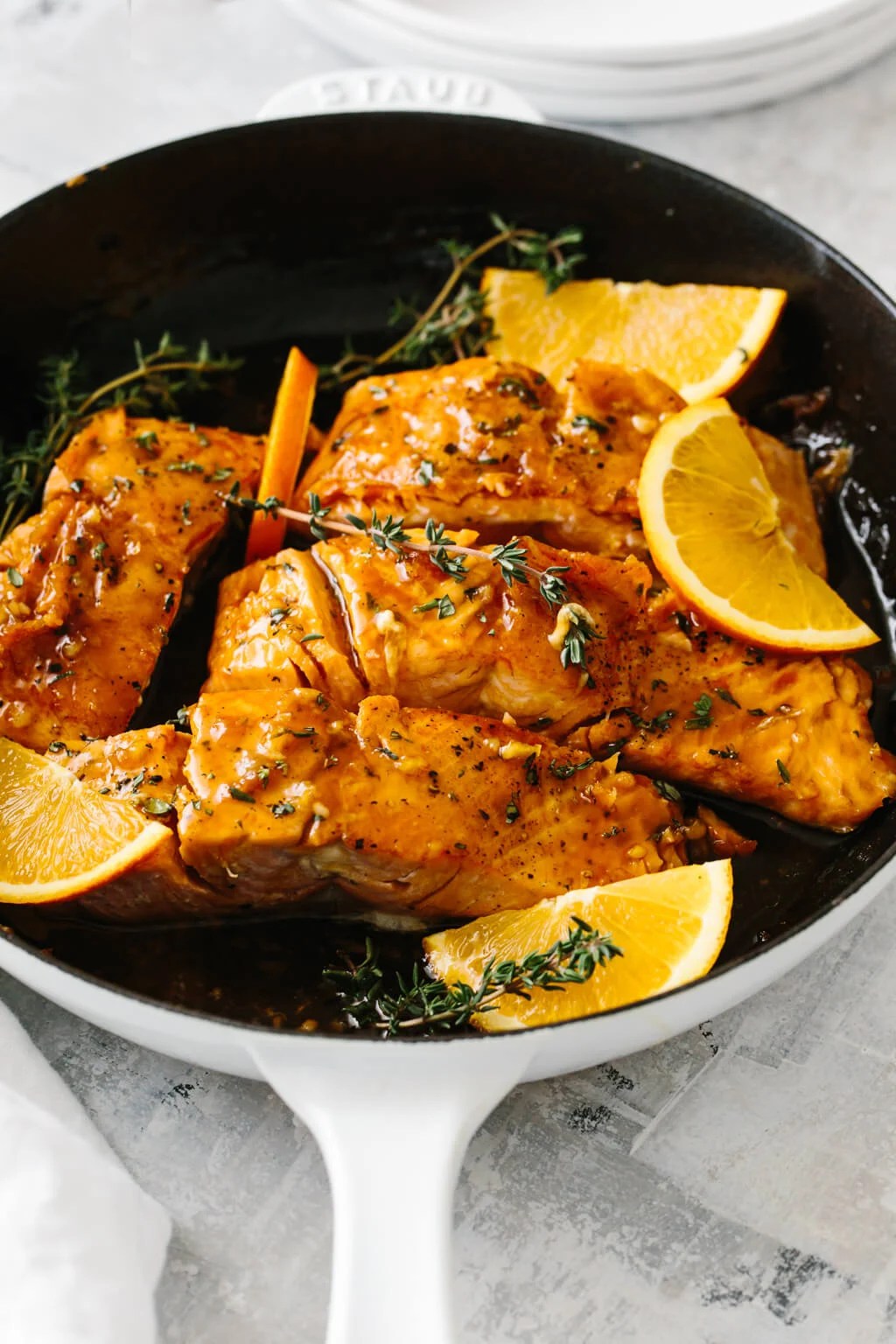 Four salmon filets in a pan with orange slices and thyme on top.