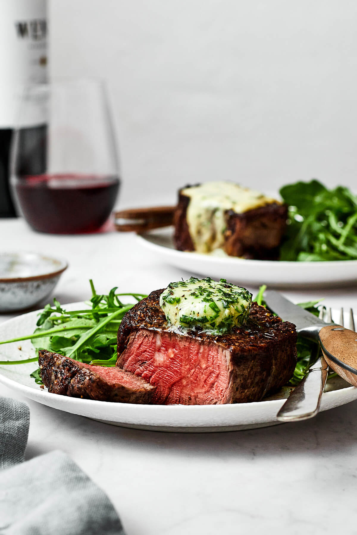 A plate of filet mignon next to a glass of wine