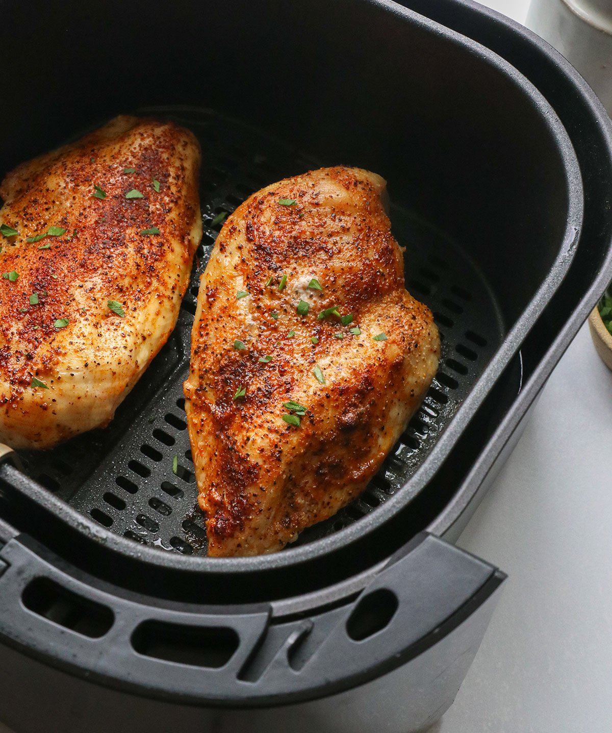 chicken breasts topped with parsley in an air fryer.