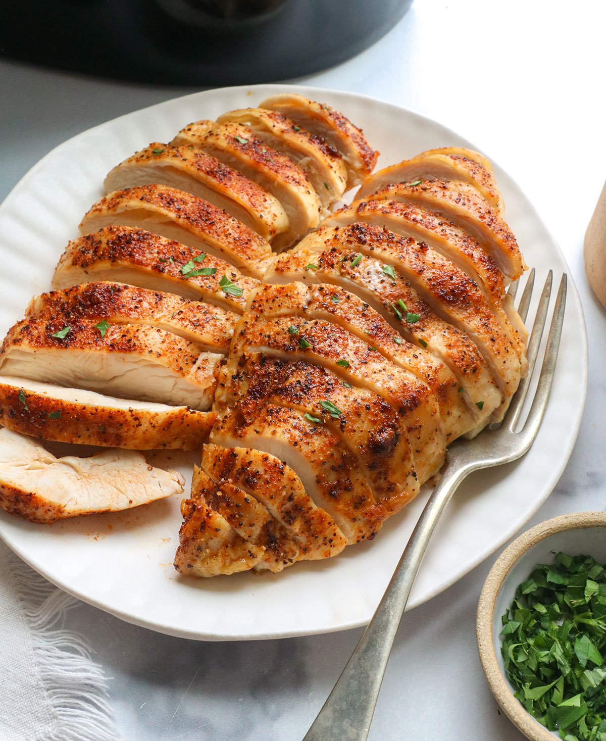 two chicken breasts sliced near an air fryer.