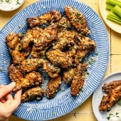 hand grabbing lemon garlic parmesan chicken wings off of platter