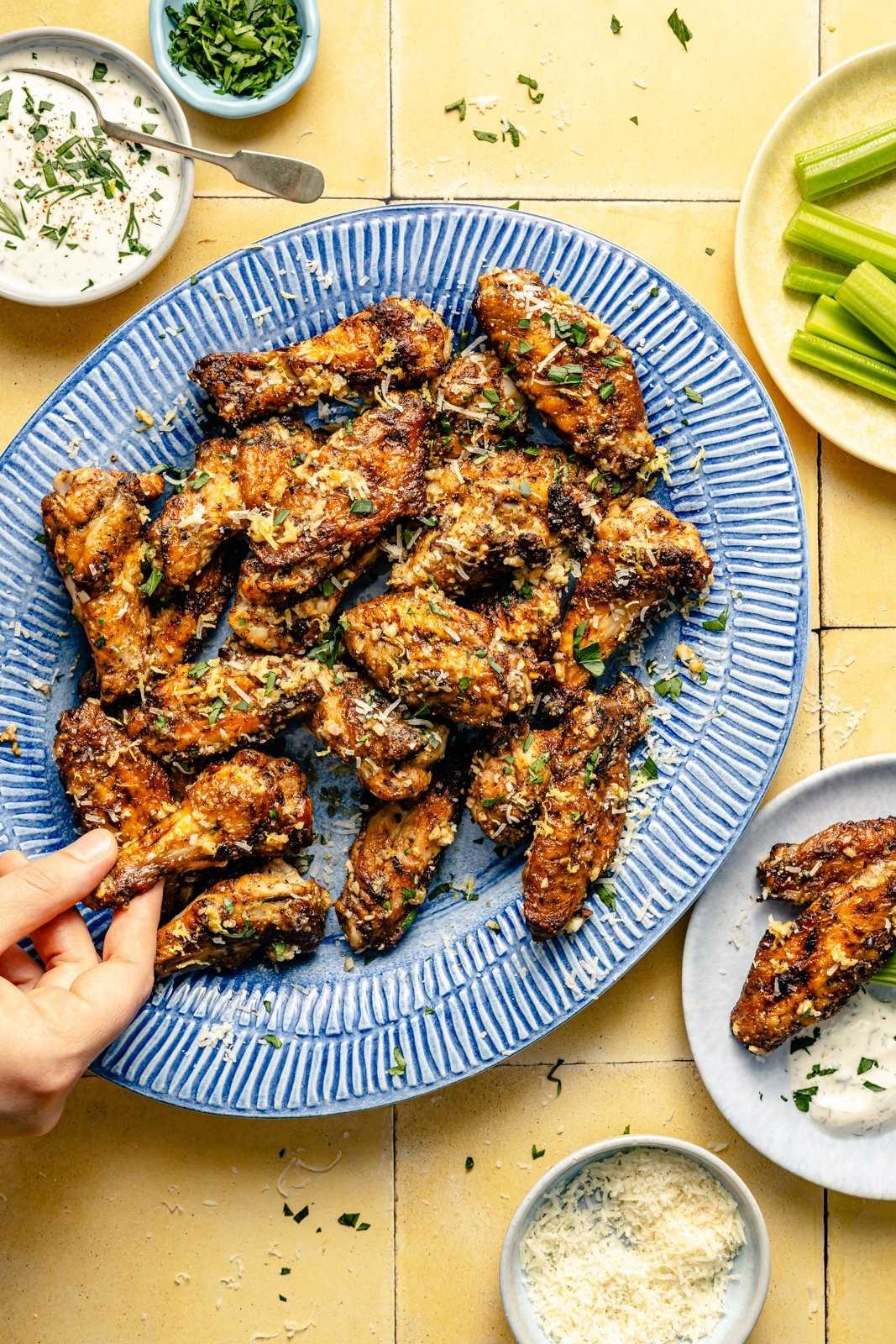 hand grabbing lemon parmesan chicken wings off of a platter