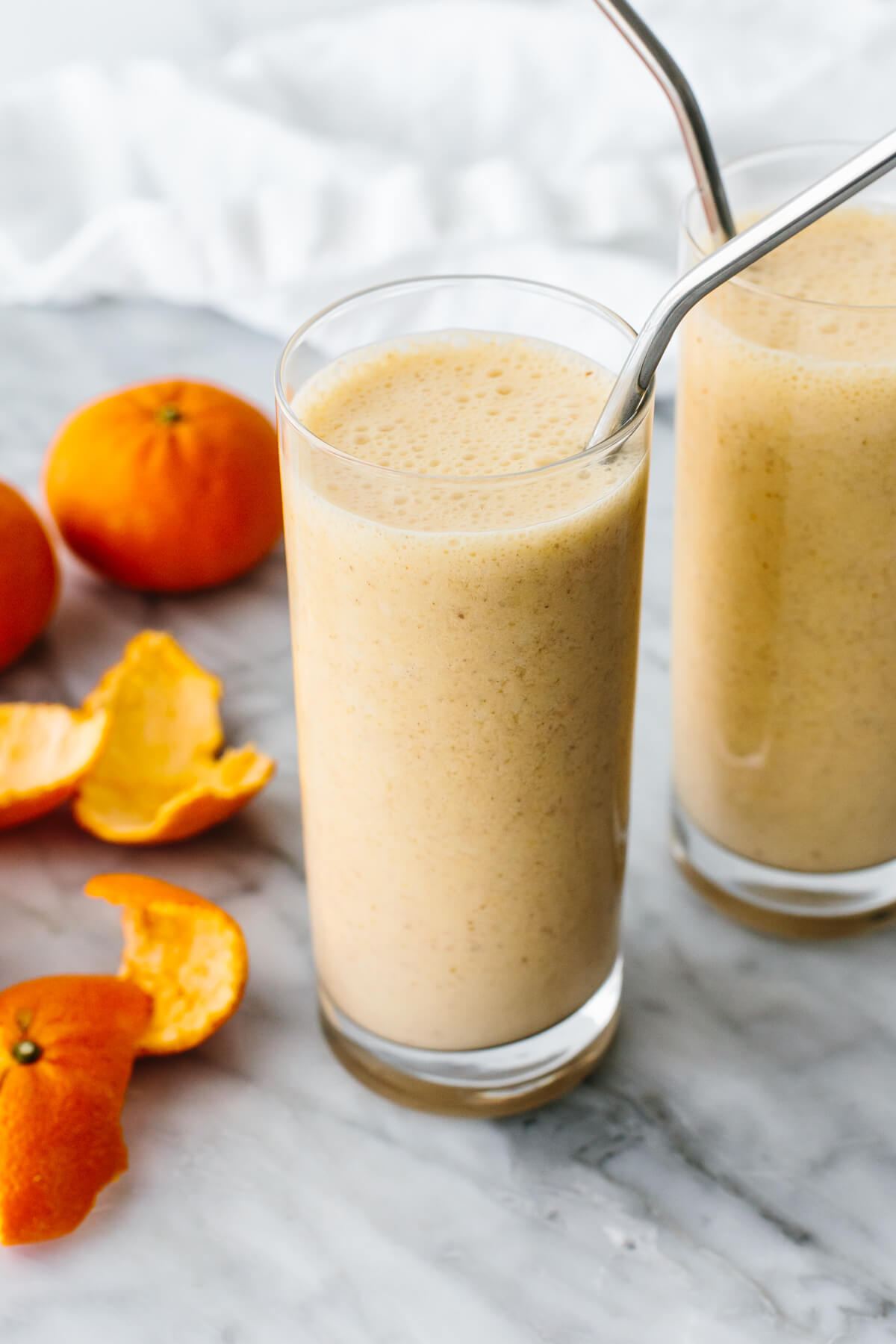 Mandarin breakfast smoothie in a glass next to mandarin oranges.