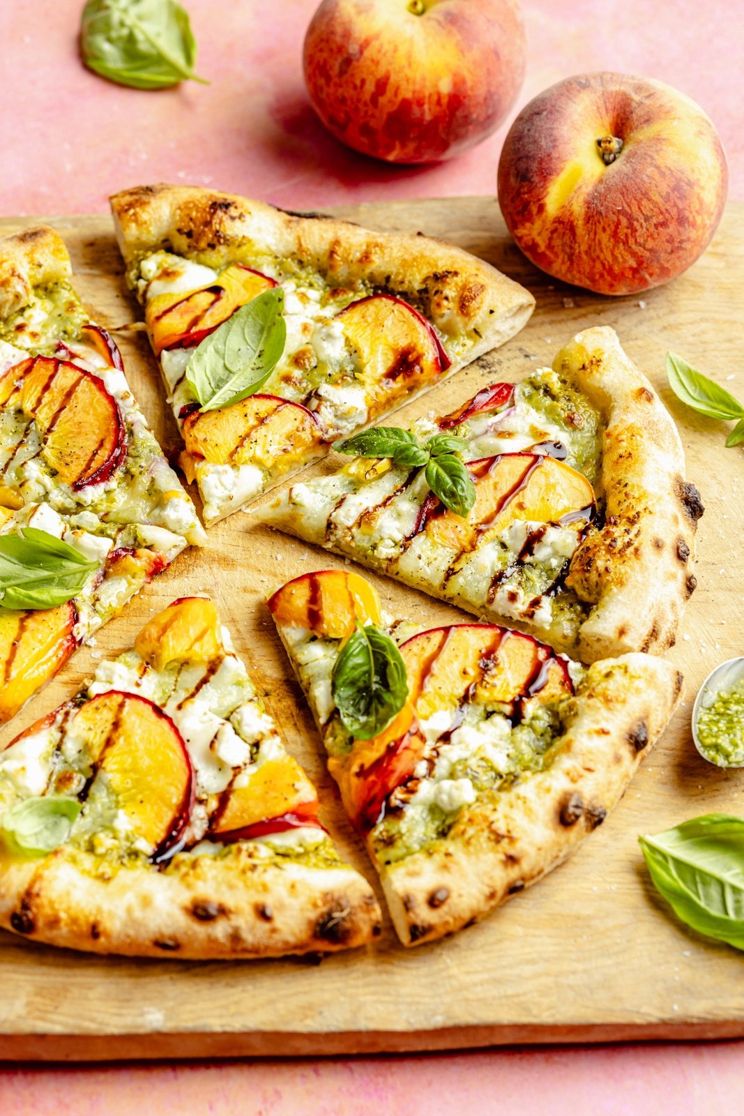 summer peach pizza with pesto and basil sliced on a wooden board