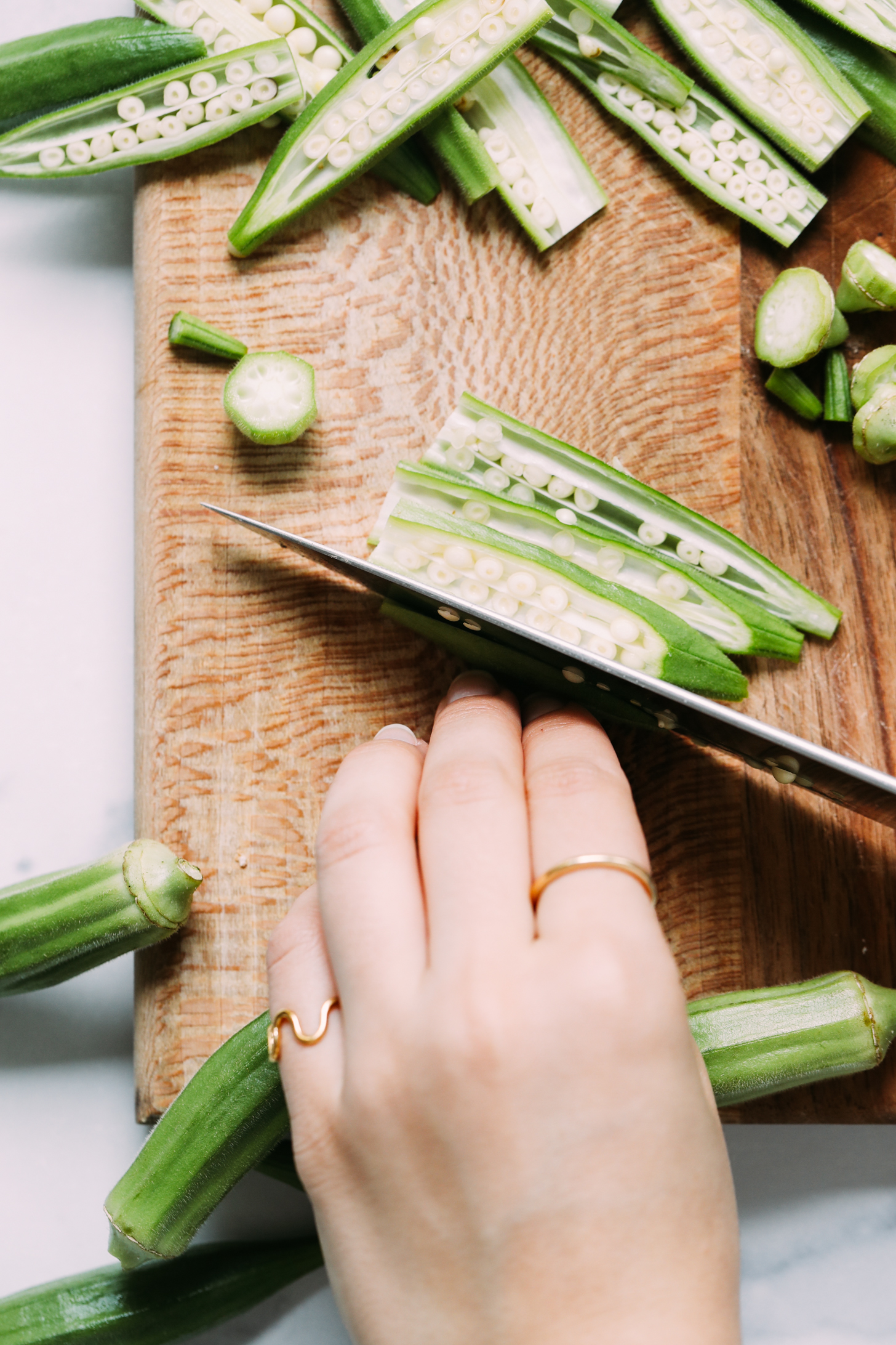 Using a chef's knife to thinly slice okra lengthwise