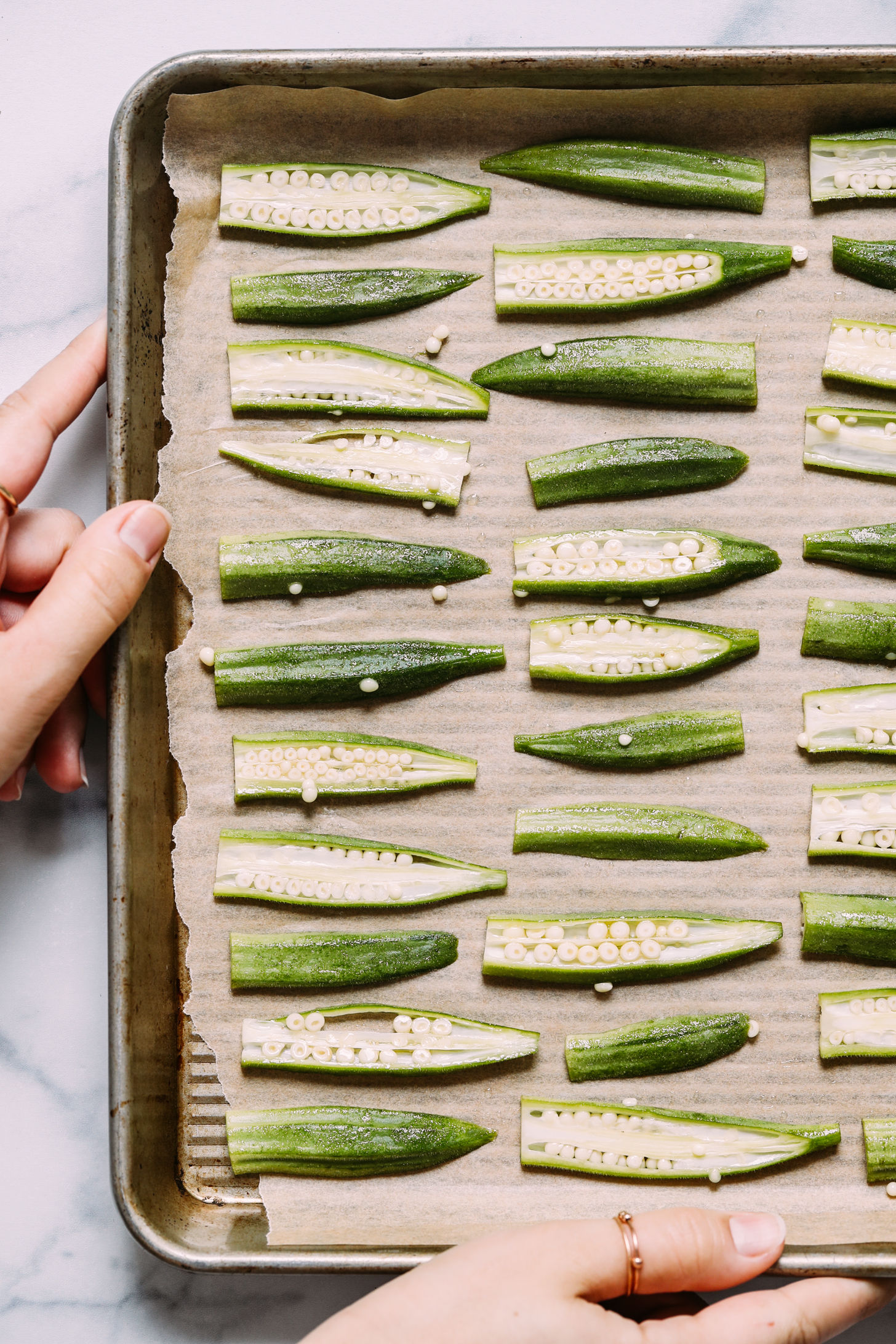 Thinly sliced okra on a baking sheet before being put in the oven