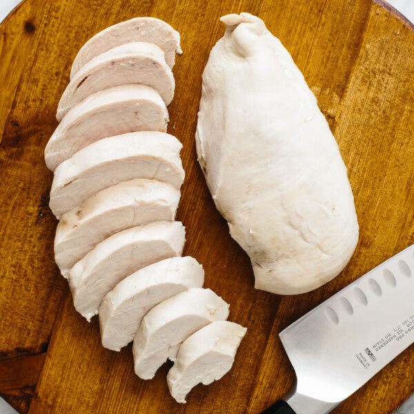 Poached chicken on a cutting board, with one breast sliced up.