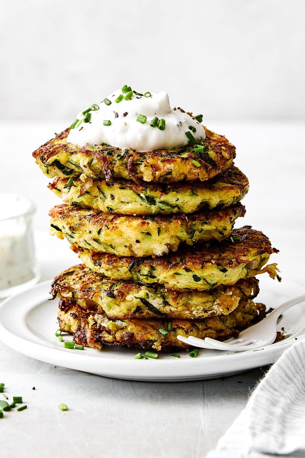 Zucchini fritters piled on a plate with yogurt sauce.