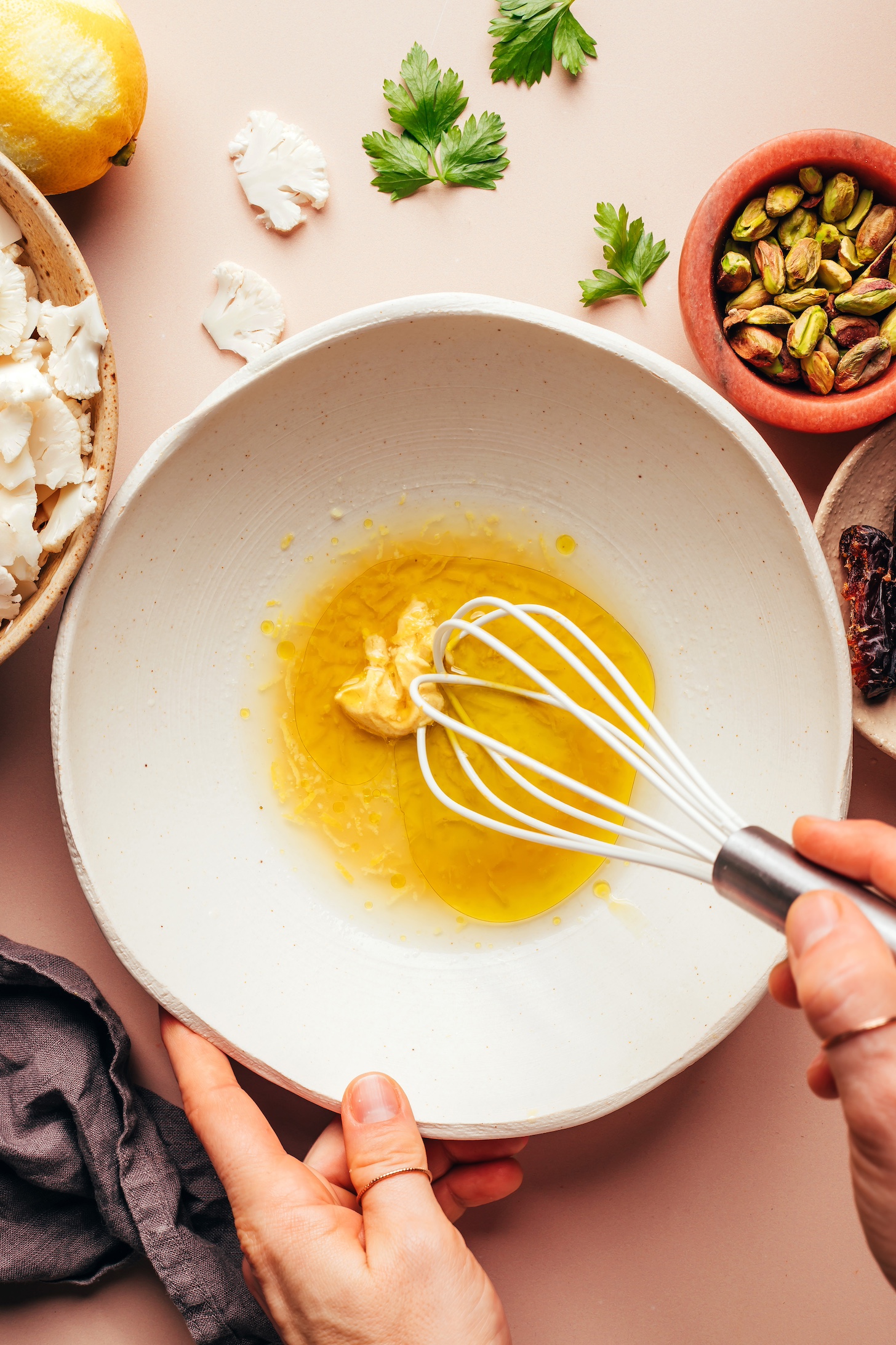 Using a whisk to mix olive oil, lemon juice, lemon zest, maple syrup, Dijon mustard, and salt in a bowl