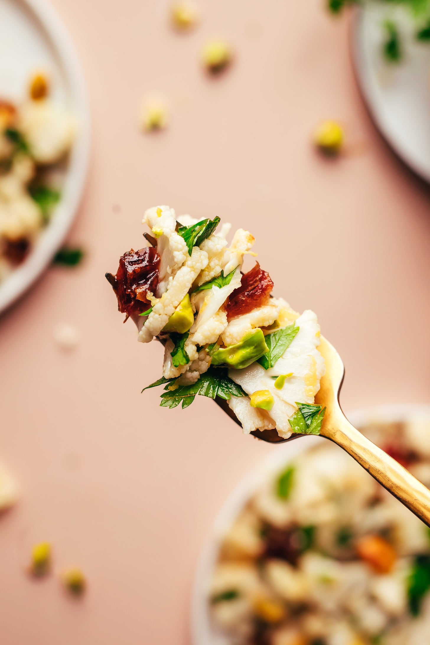Fork with a bite of cauliflower salad with pieces of dates, pistachios, and parsley