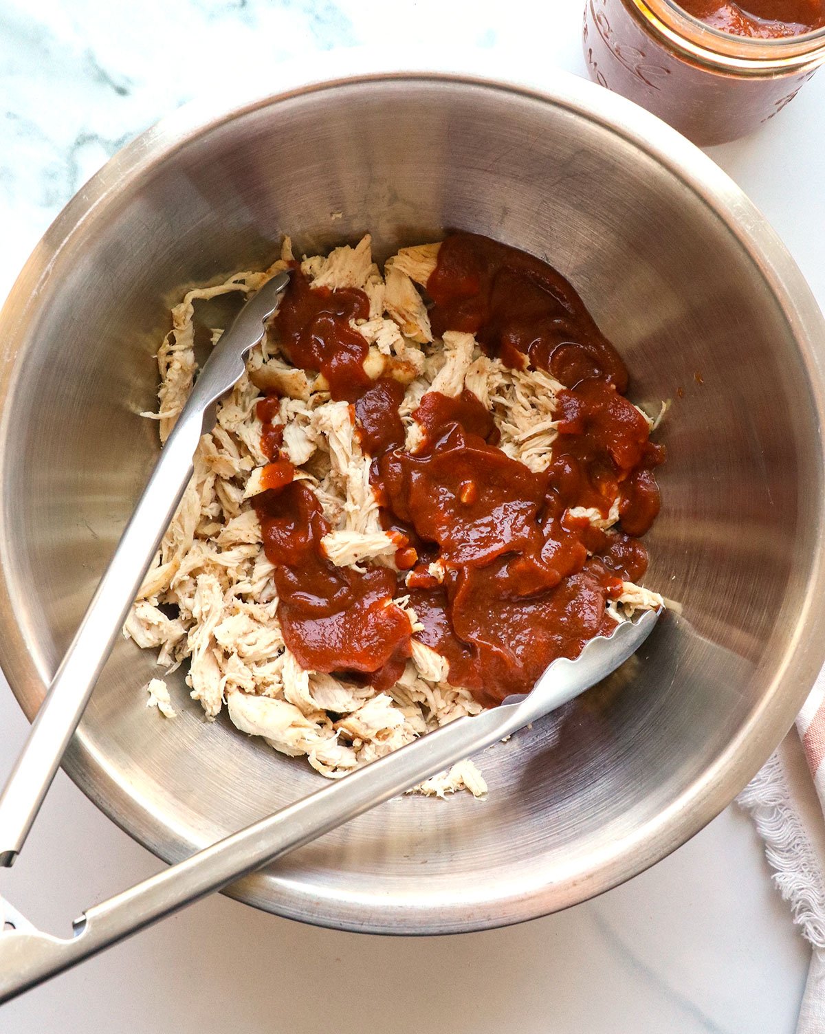 healthy BBQ sauce added to shredded chicken with tongs.