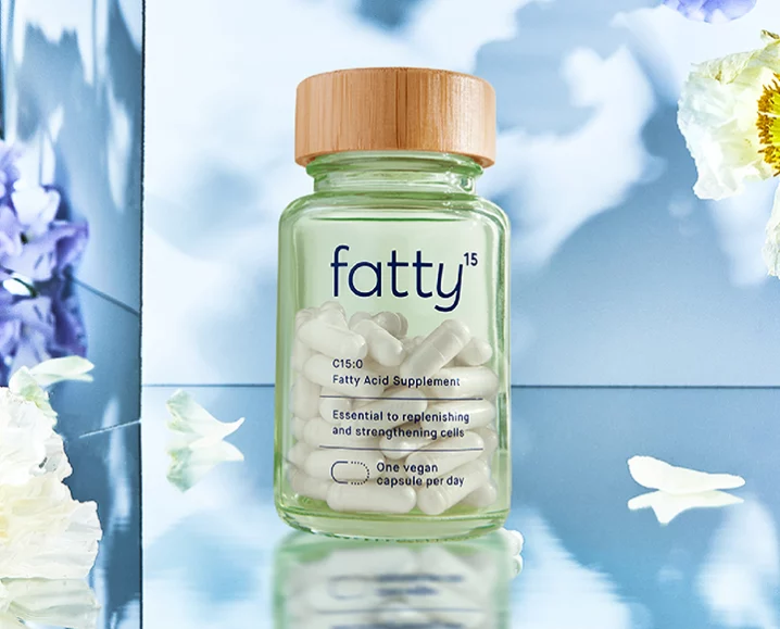 Bottle of Fatty15 C15:0 fatty acid supplement with wooden cap, surrounded by flowers, symbolizing cellular health and graceful aging