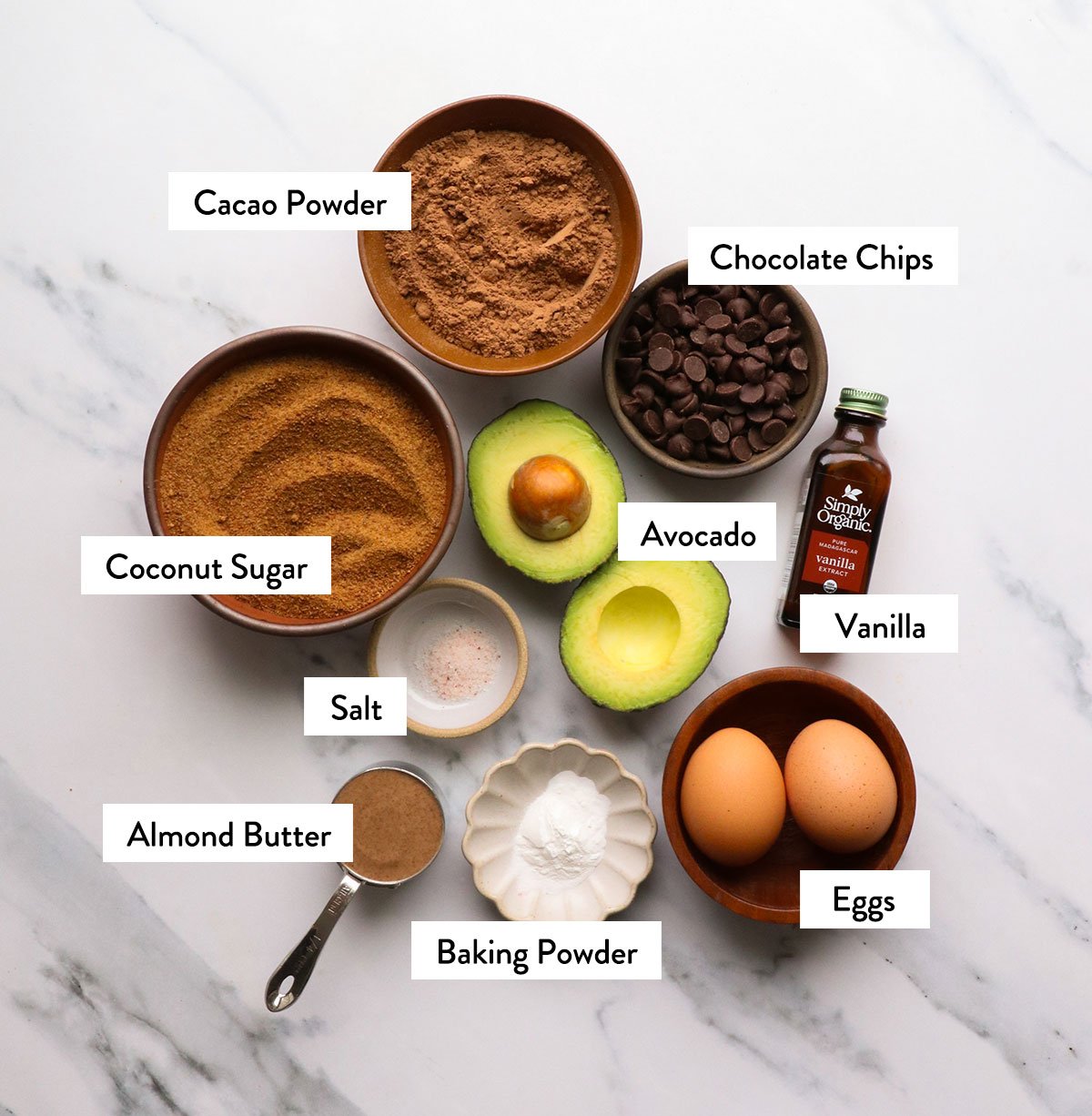 avocado, cacao powder, coconut sugar, eggs, and vanilla labeled in a white surface.