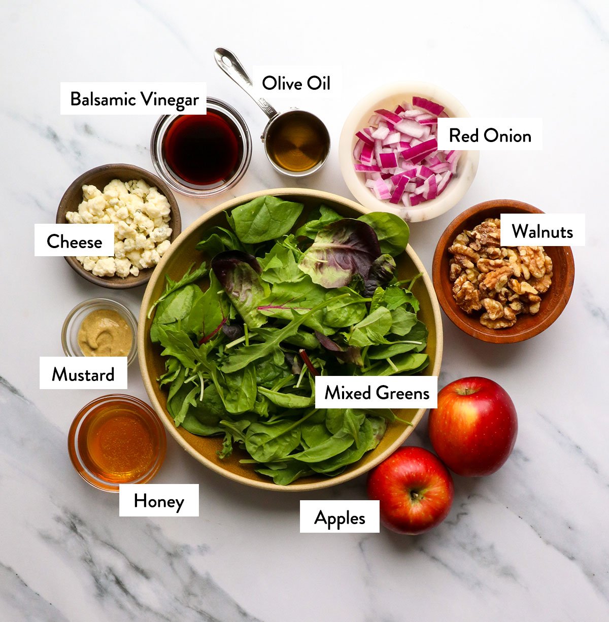 mixed greens, apples, walnuts, crumbled cheese and dressing labeled on a white surface.