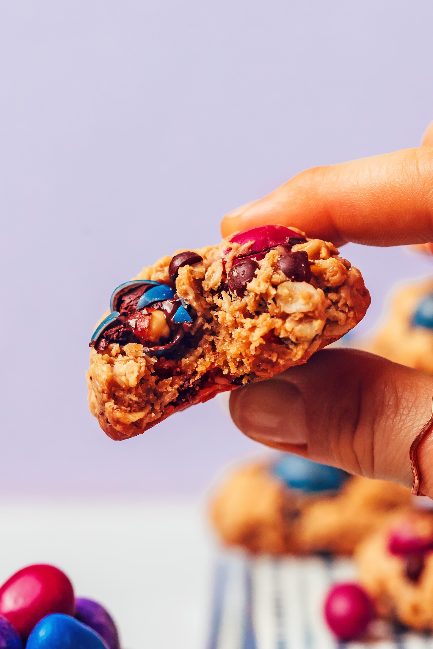 Fingers holding up a partially eaten gluten-free monster cookie to show the chewy inner texture