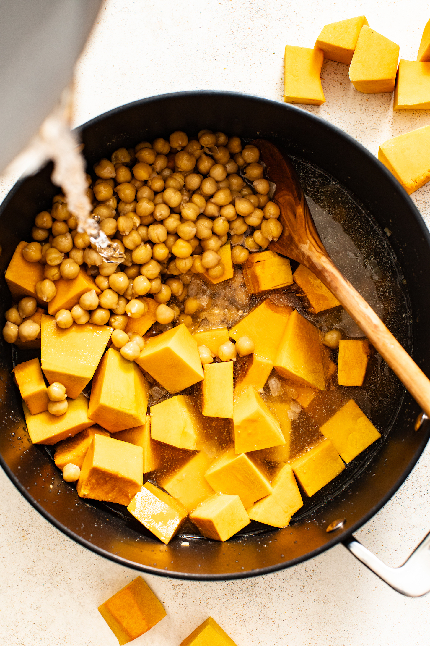 Pouring water into a pot with chickpeas and kabocha squash