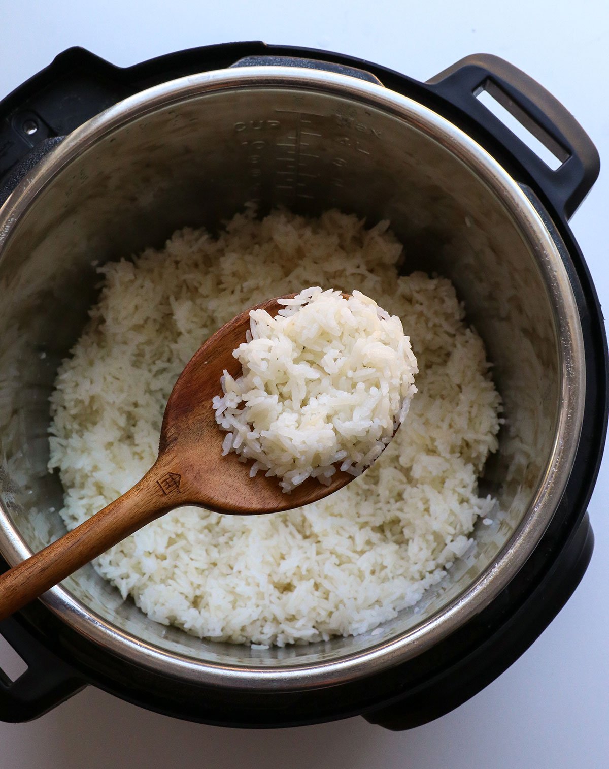 wooden spoon holding white rice over the instant pot. 