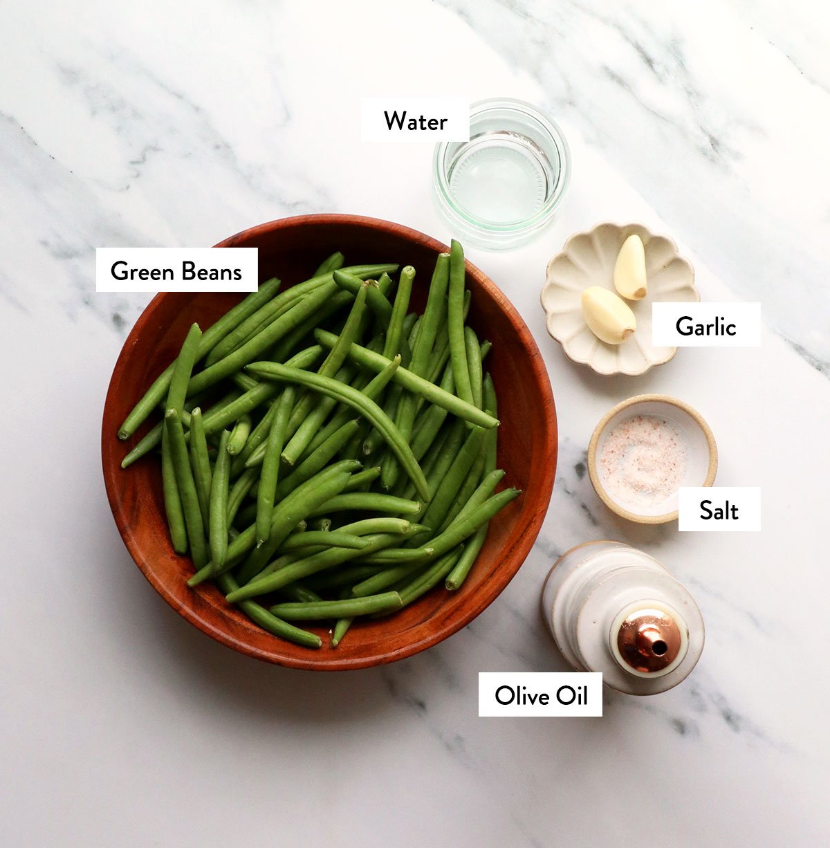 green beans, salt, garlic, and olive oil labeled on a white surface.