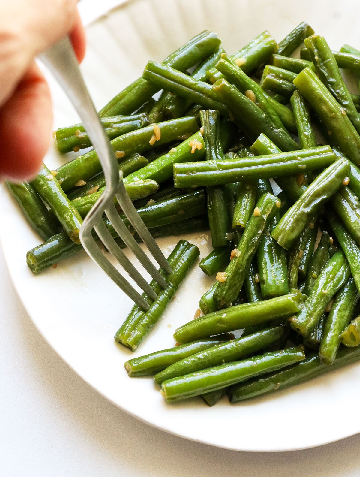 sauteed green beans on a white plate with a fork grabbing one.