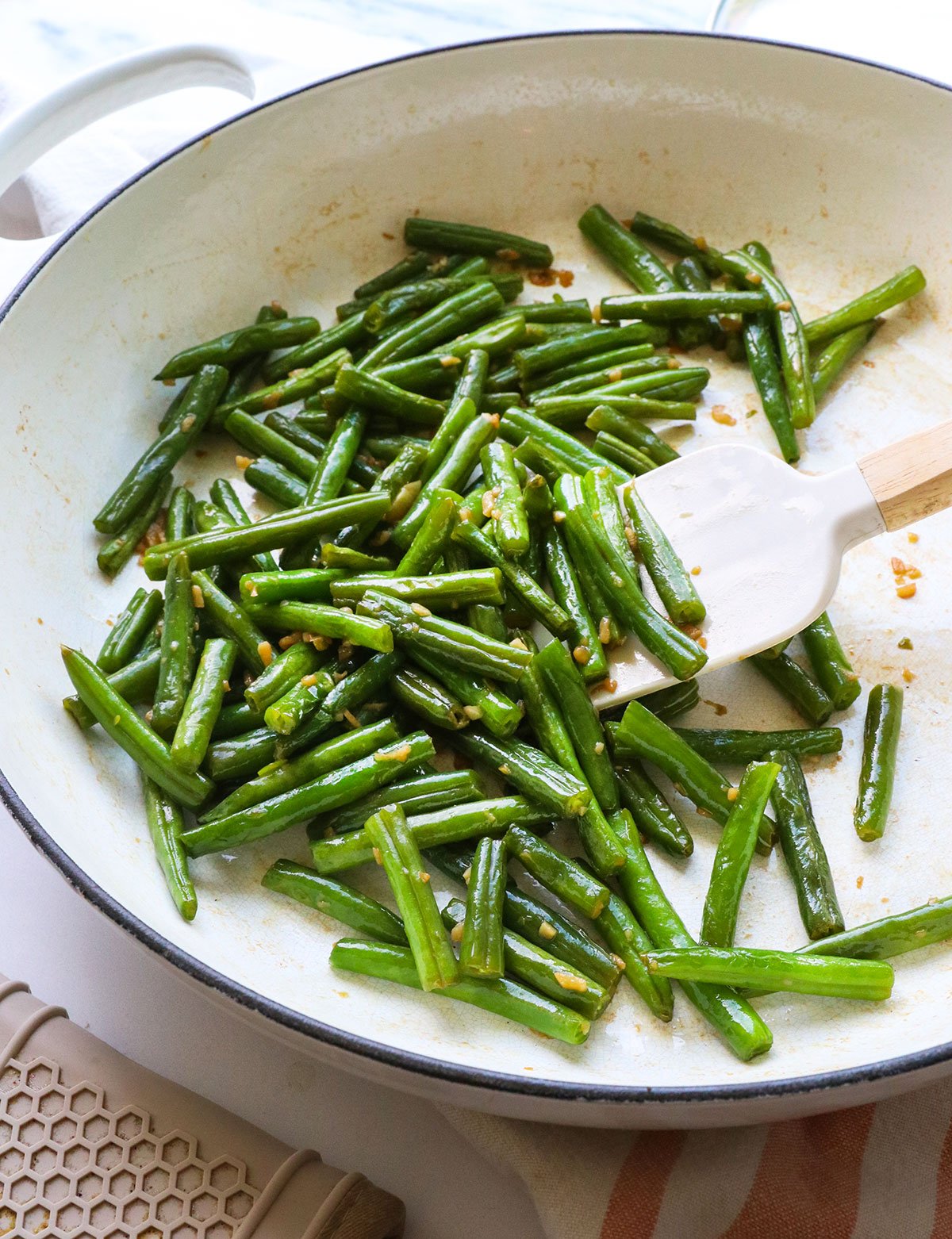 sauteed green beans in a white skillet with spatula.