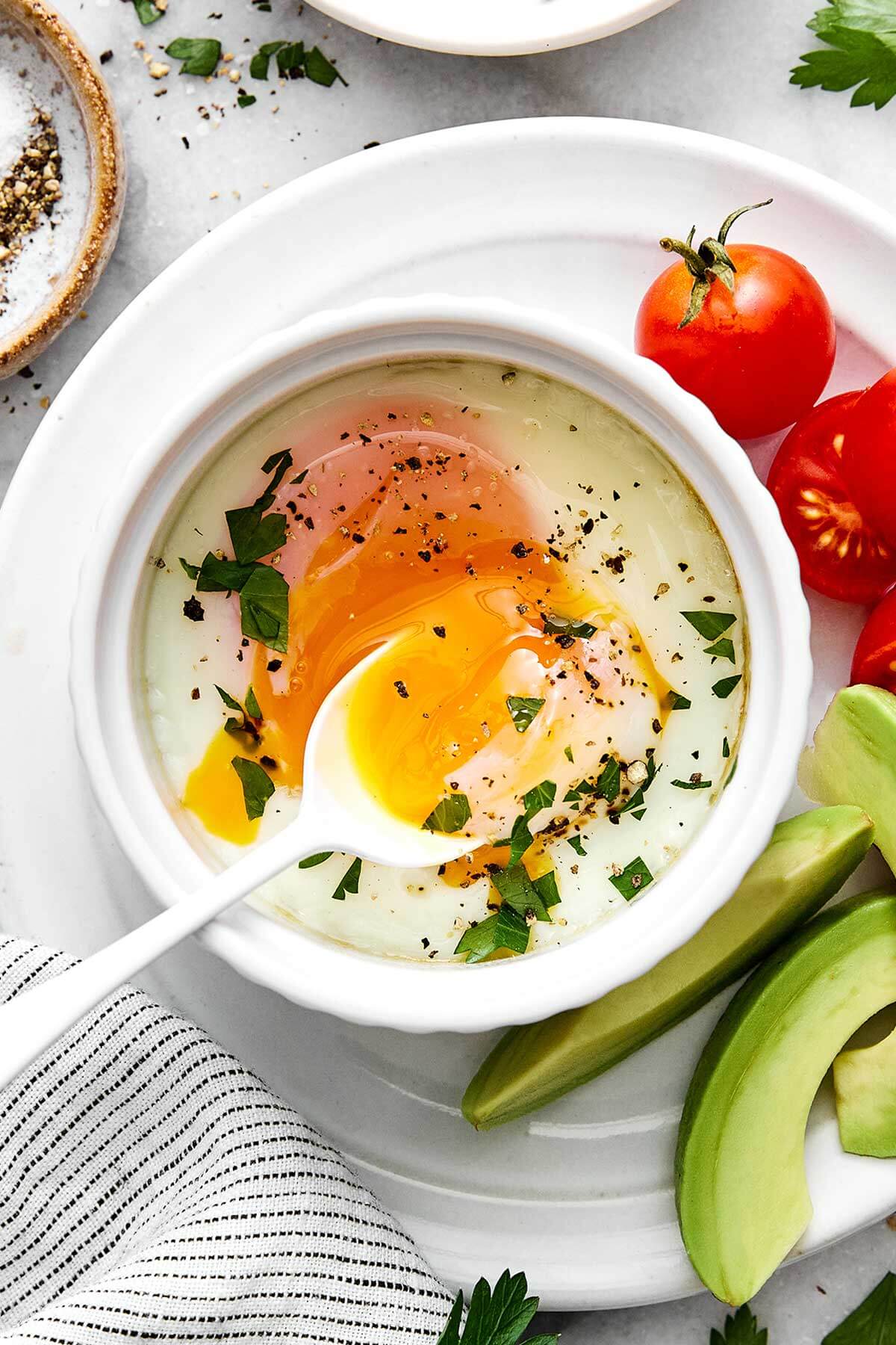 Baked eggs on a plate with tomatoes and avocado is one way to cook eggs.