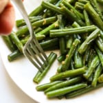 sauteed green beans on a white plate with a fork grabbing one.