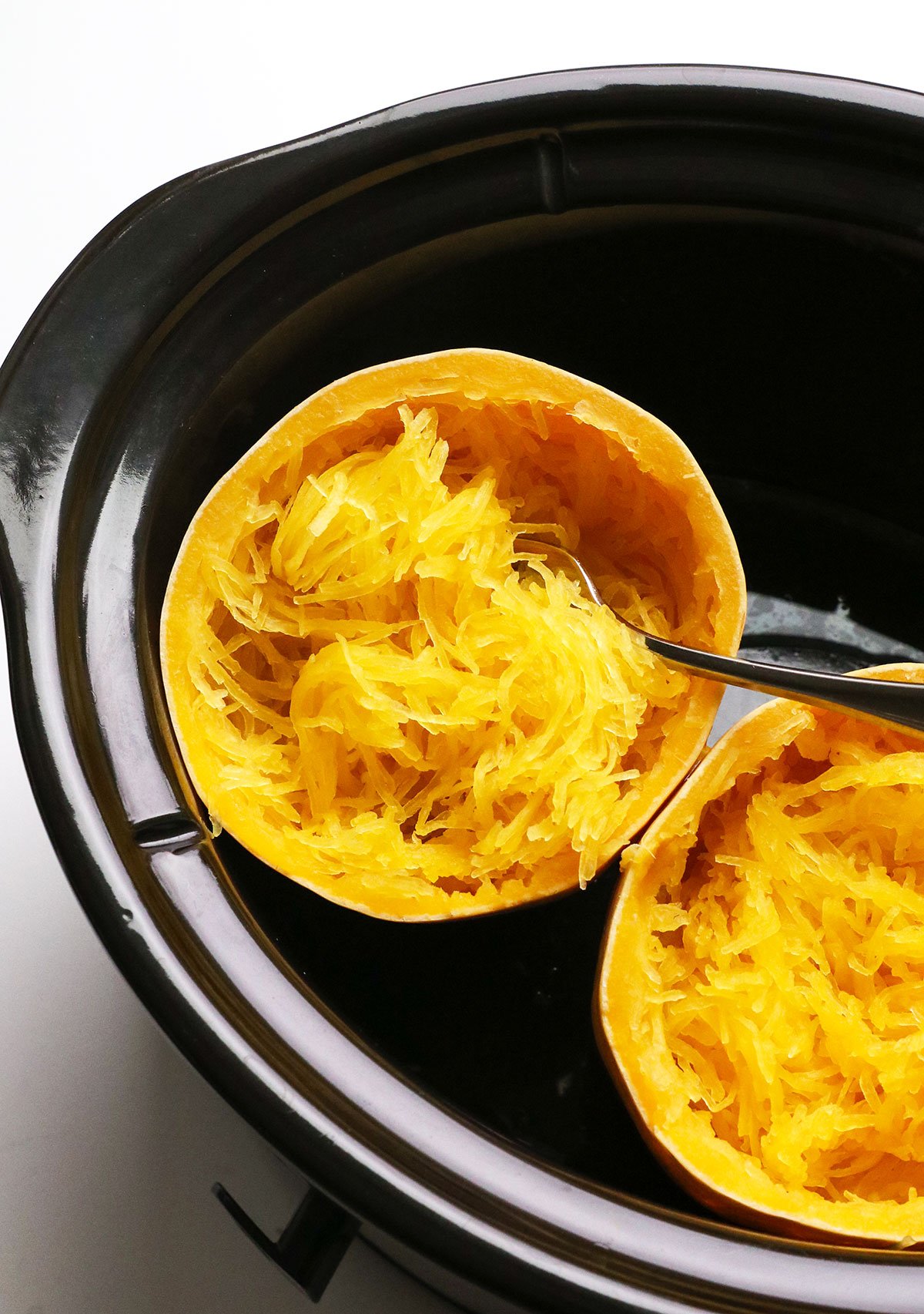 spaghetti squash cooked in a black slow cooker with a fork. 