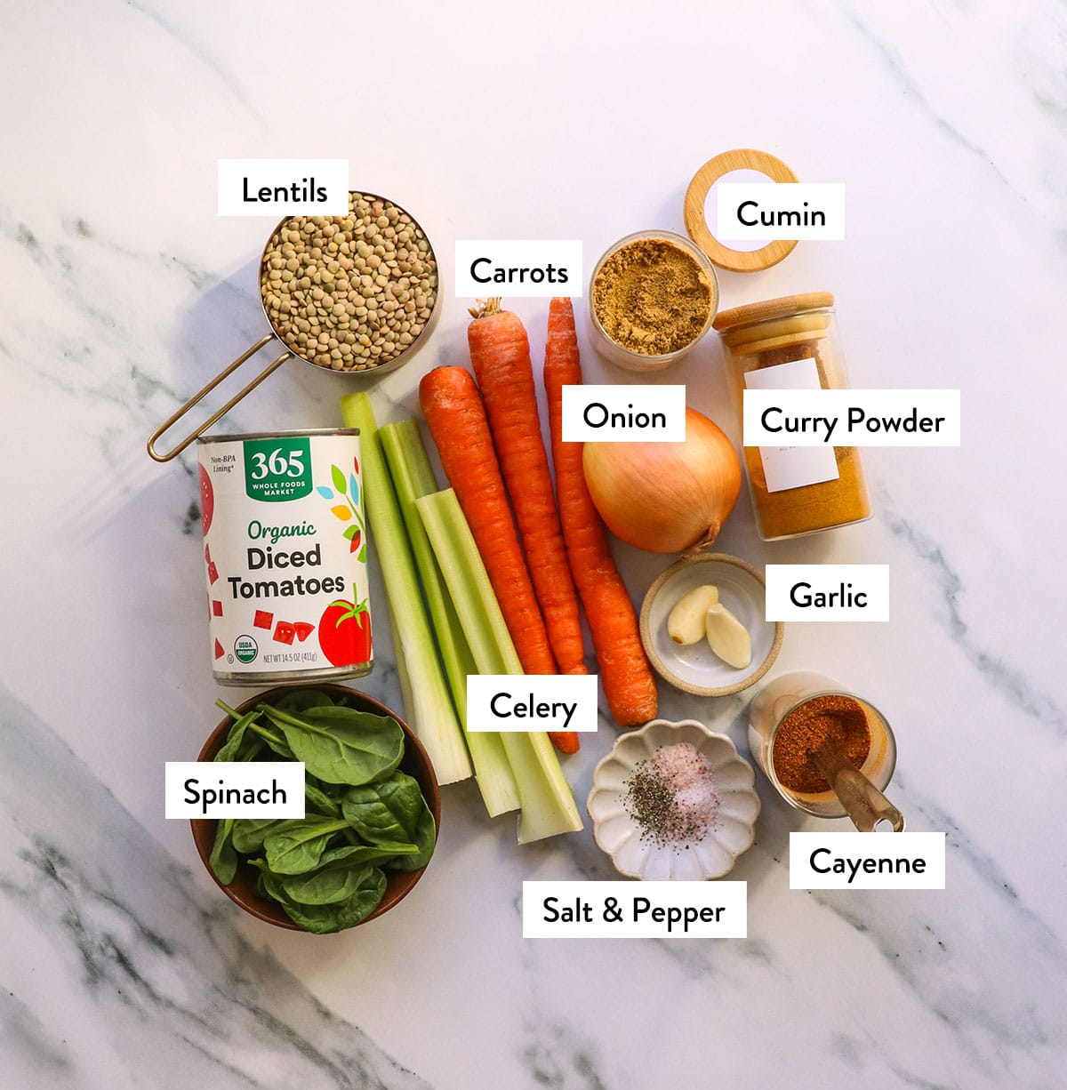 carrot, celery, onion, lentils, spinach, and spices labeled on a white surface. 