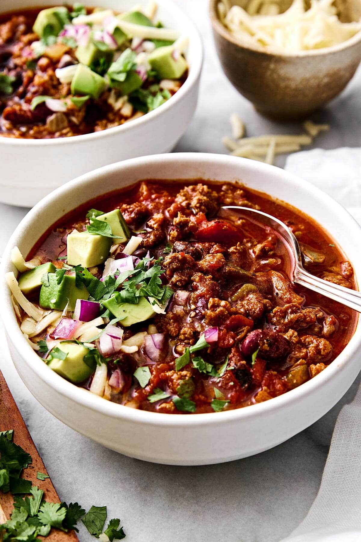A white bowl of beef chili with toppings.