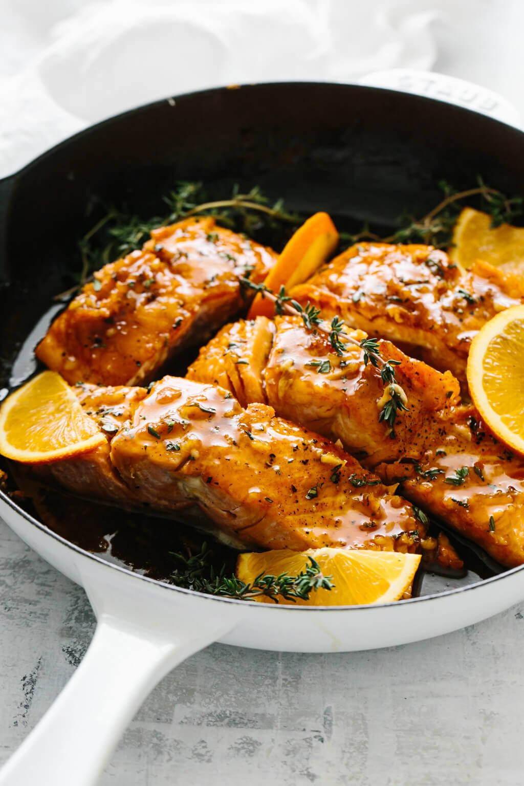 Four salmon filets in a pan with orange slices and thyme on top.