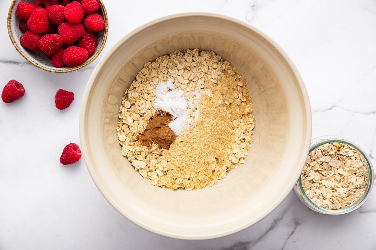 Dry ingredients for baked oatmeal including oats, flaxseed, cinnamon and baking powder in bowl.