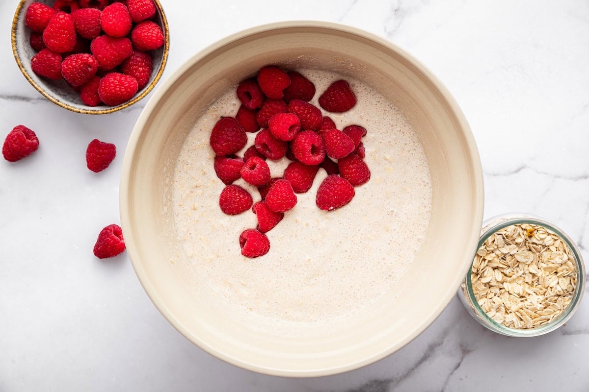 Fresh raspberries being added to a mixing bowl with the baked oatmeal mixture.