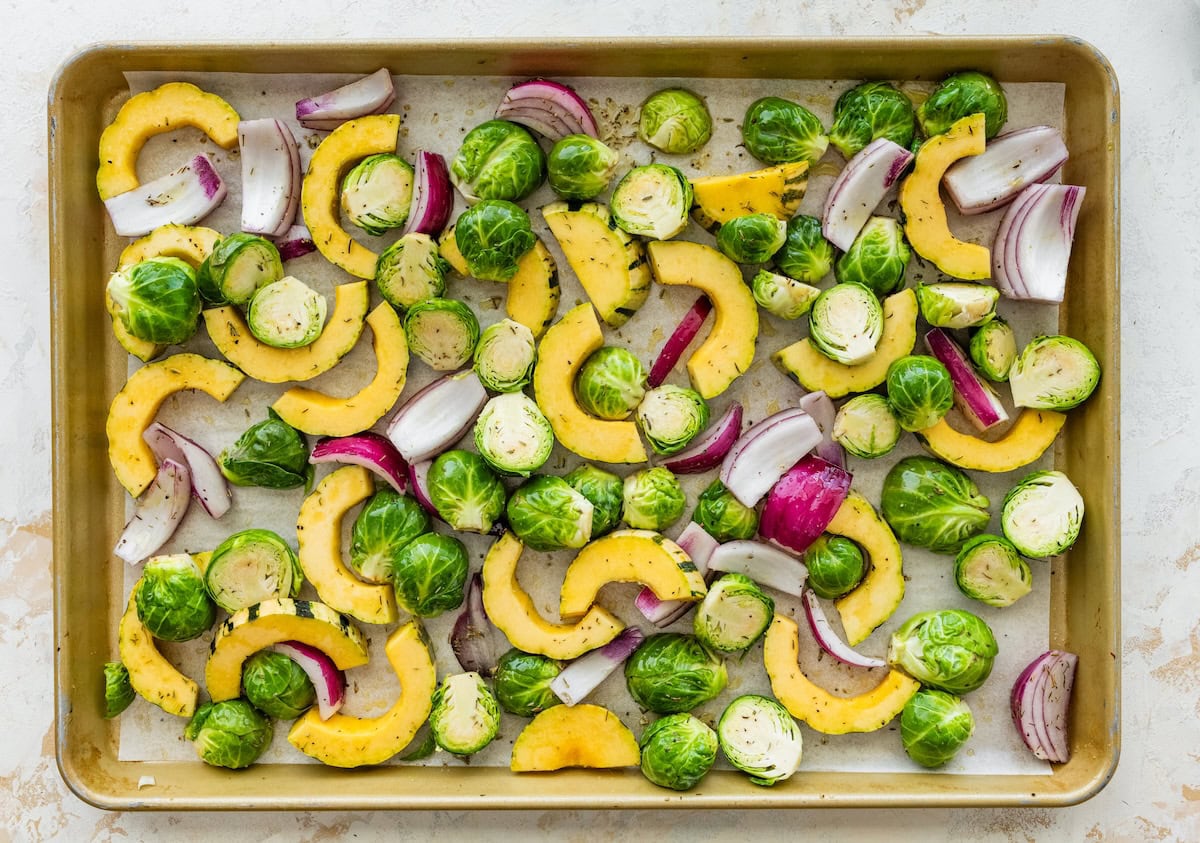 Brussels sprouts, delicata squash, and red onion tossed on a sheet pan before roasting.