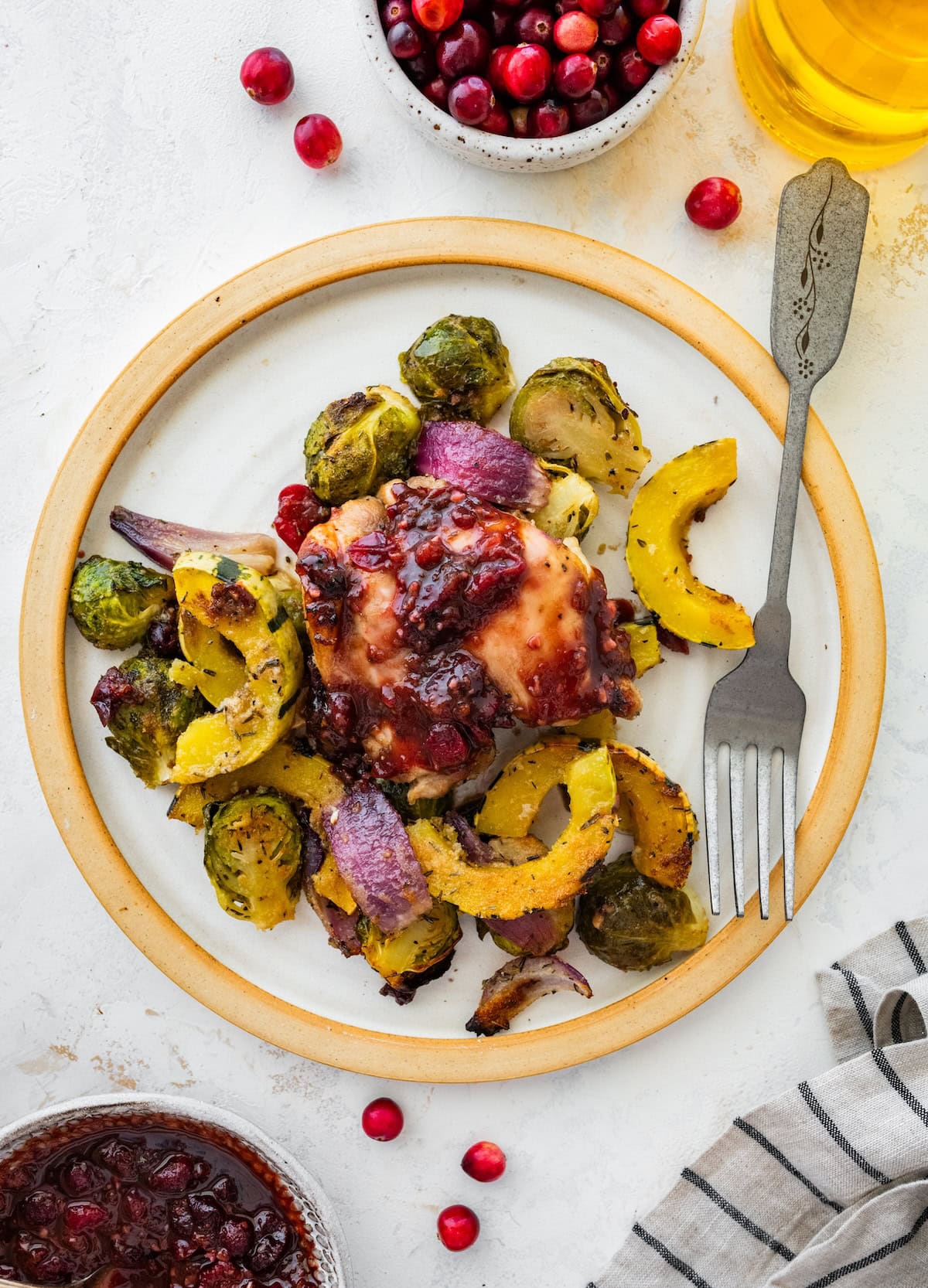 Plated cranberry balsamic chicken with roasted Brussels sprouts and delicata squash on a white plate.