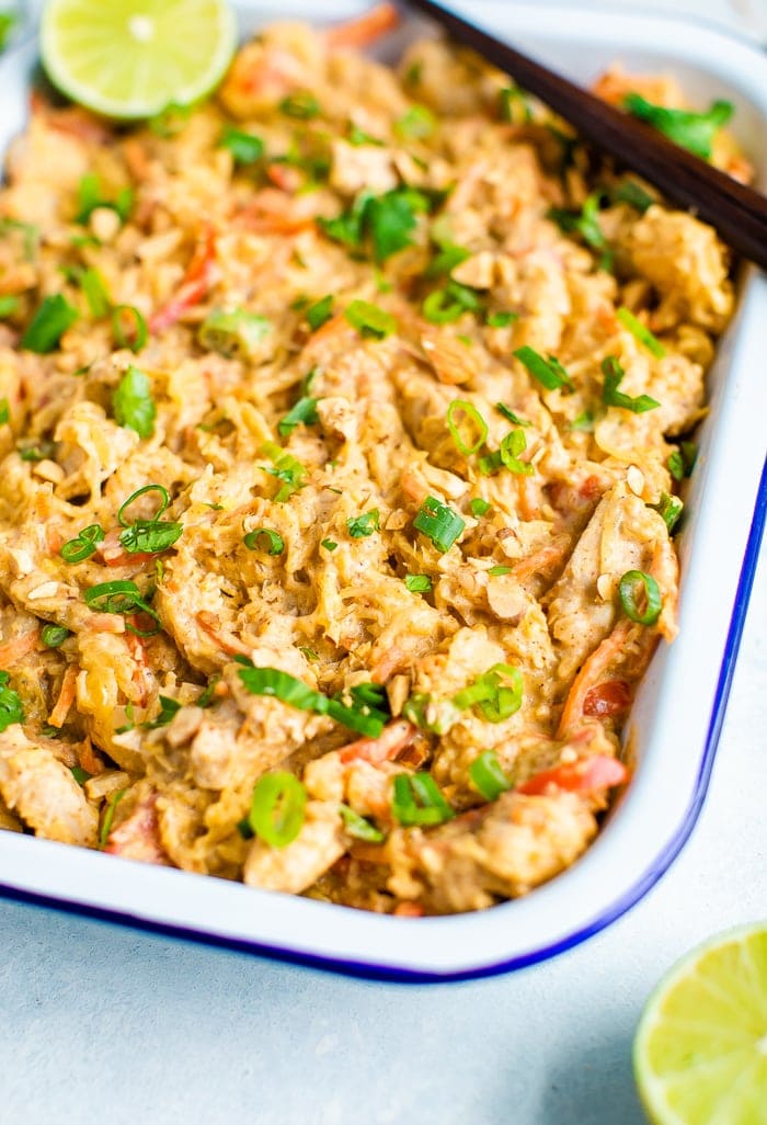 Rectangle serving tray full of spaghetti squash pad thai and topped with cilantro, peanuts, green onions and lime. Chop sticks are resting on the edge of the tray.