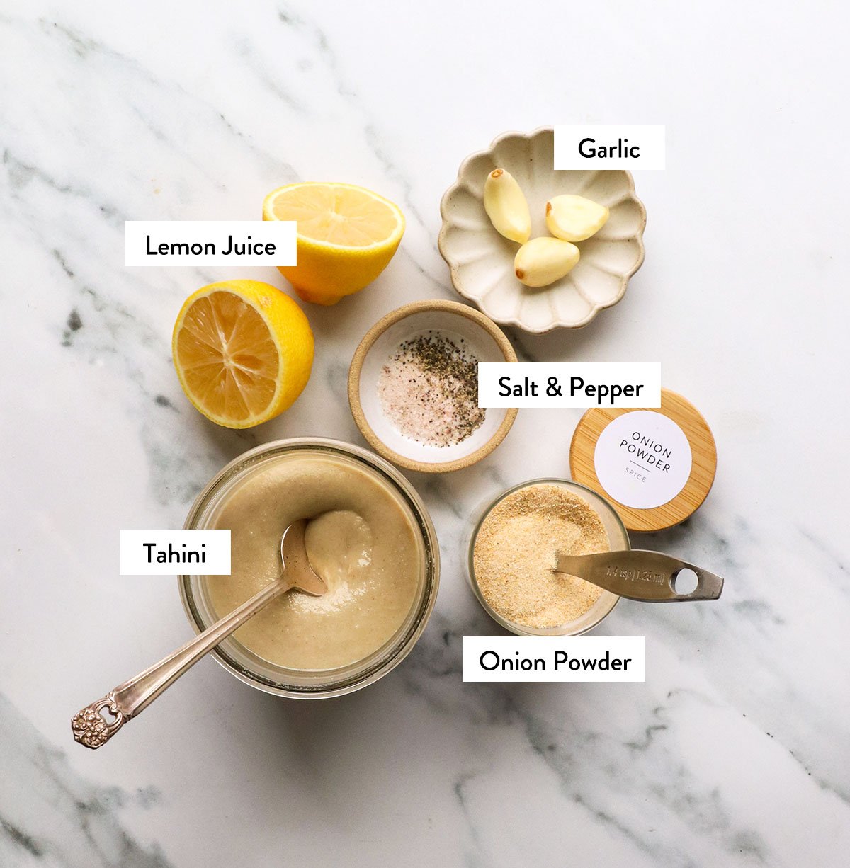 tahini, lemon, garlic, and spices labeled on a white surface. 