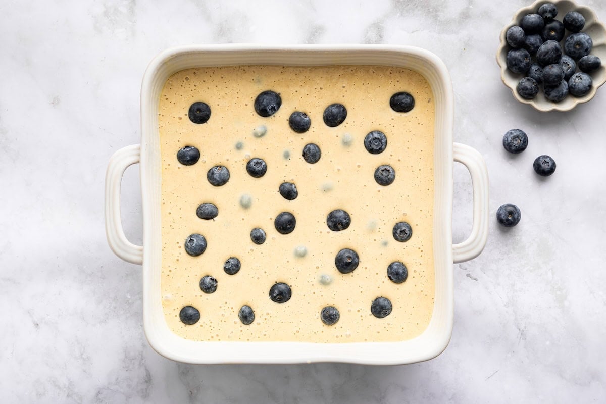 Blueberry cottage cheese breakfast bake batter in a white baking dish topped with blueberries before baking.