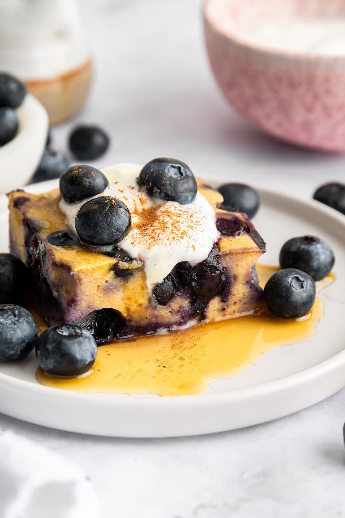 Slice of blueberry cottage cheese breakfast bake topped with blueberries and syrup on a white plate.