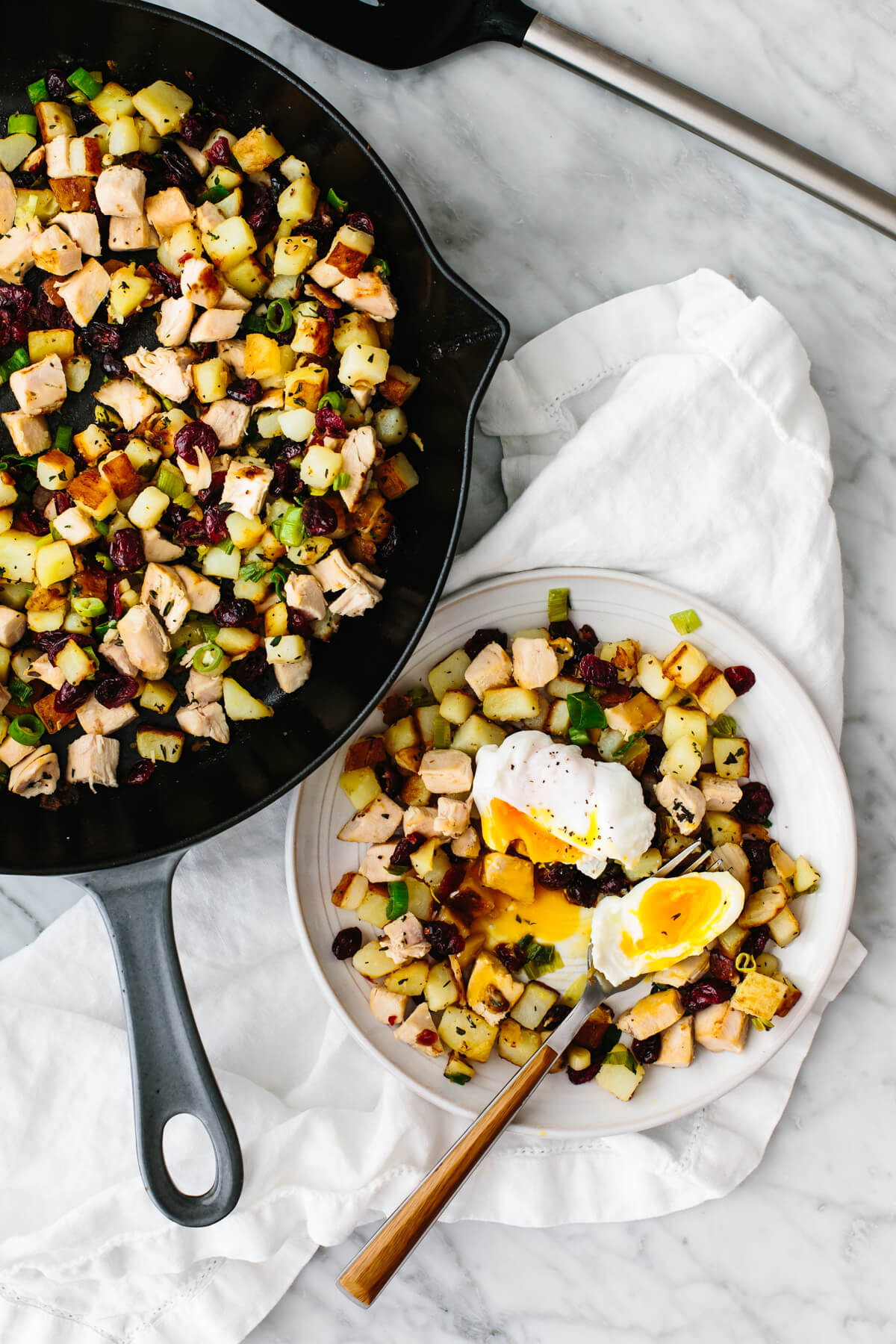 A plate of turkey cranberry hash with poached egg next to saute pan.