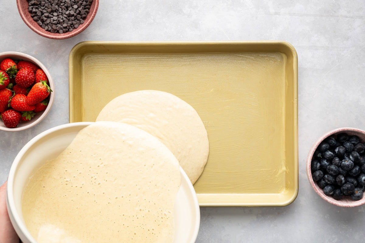 Pouring pancake batter into a greased quarter sheet pan.