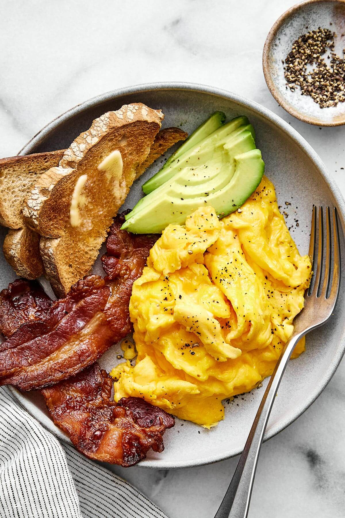 Scrambled eggs with bacon, avocado, and toast.