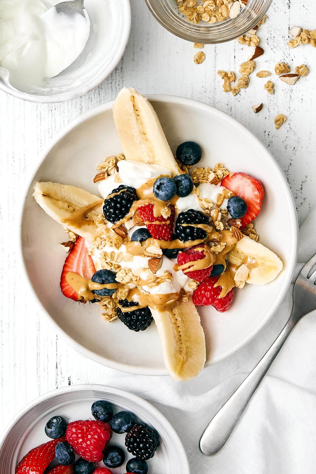 A breakfast banana split in a bowl next to toppings.